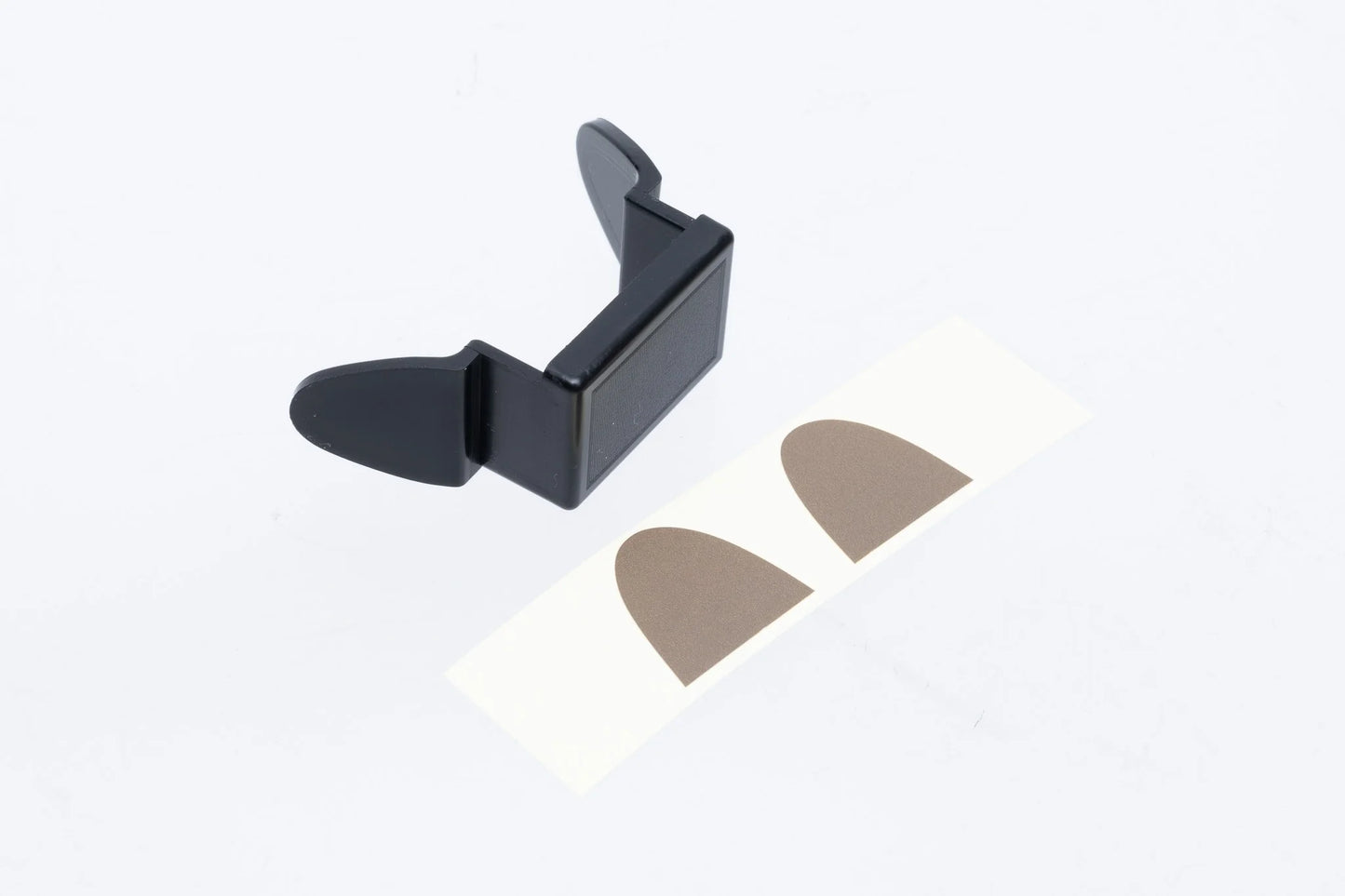 The SPARK Black Battery Compartment Cover by AIRSOFT97 shown from an angled perspective next to its included strip of two Dark Earth (DE) adhesive color seals on a white background.