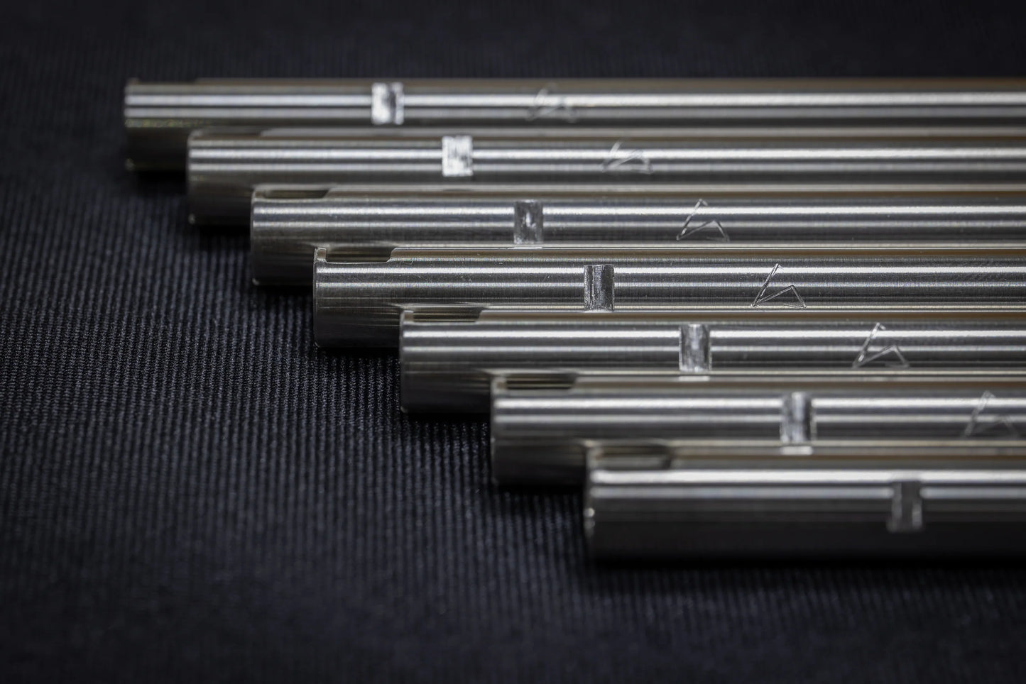 A stacked row of multiple stainless steel SPARK Hiei Kai 6.15mm inner barrels by AIRSOFT97, displaying their precision hop-up cuts and engraved geometric alignment marks on a dark textured surface.